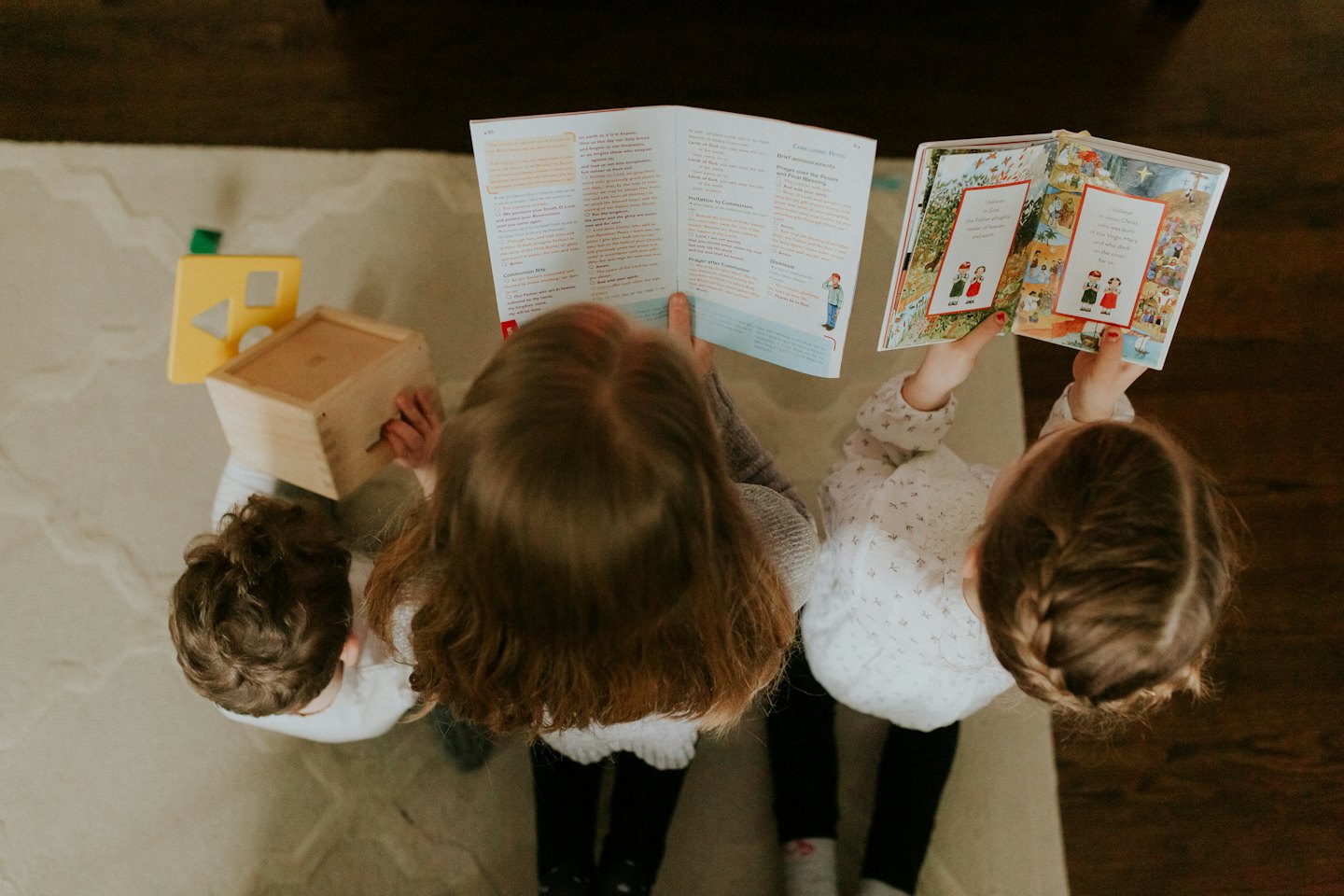 Three children reading and playing together on a rug.