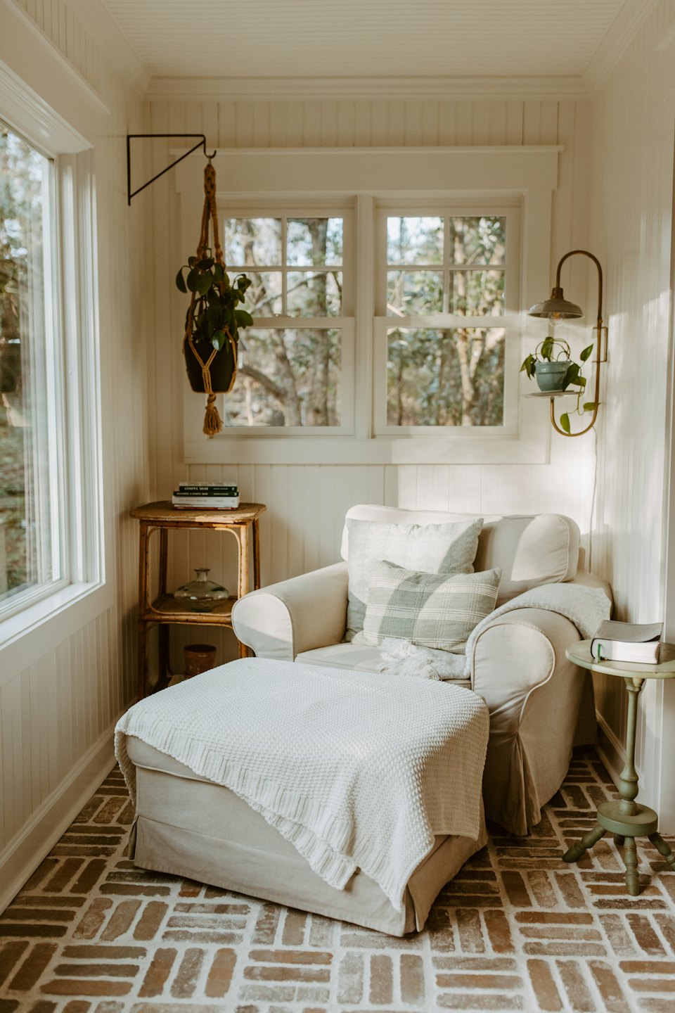 Sunlit reading nook with cream armchair, plants, and brick floor.